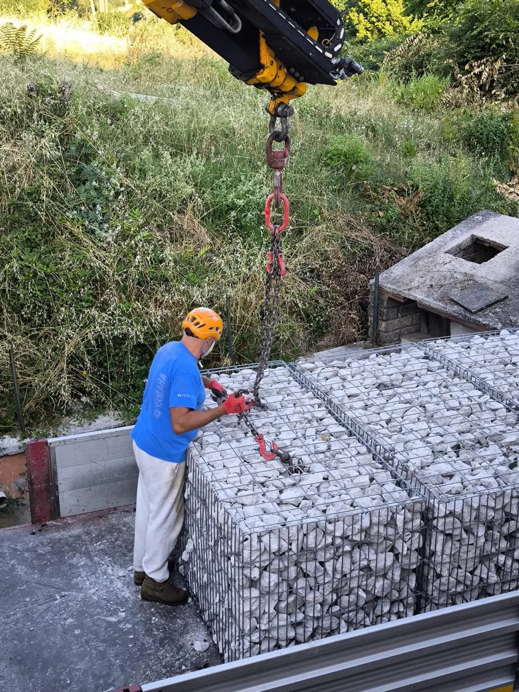 Operatore con casco e guanti durante la posa di gabbioni in pietra